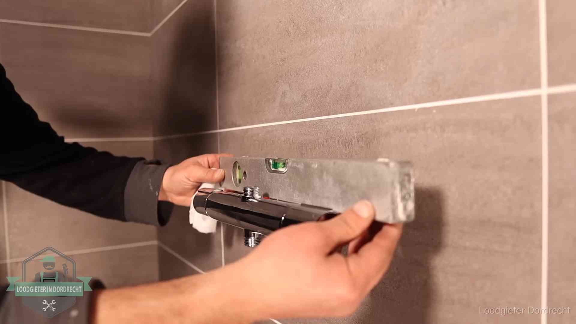 Loodgieter lijnt een douchekraan uit met een waterpas in een woning in Dordrecht