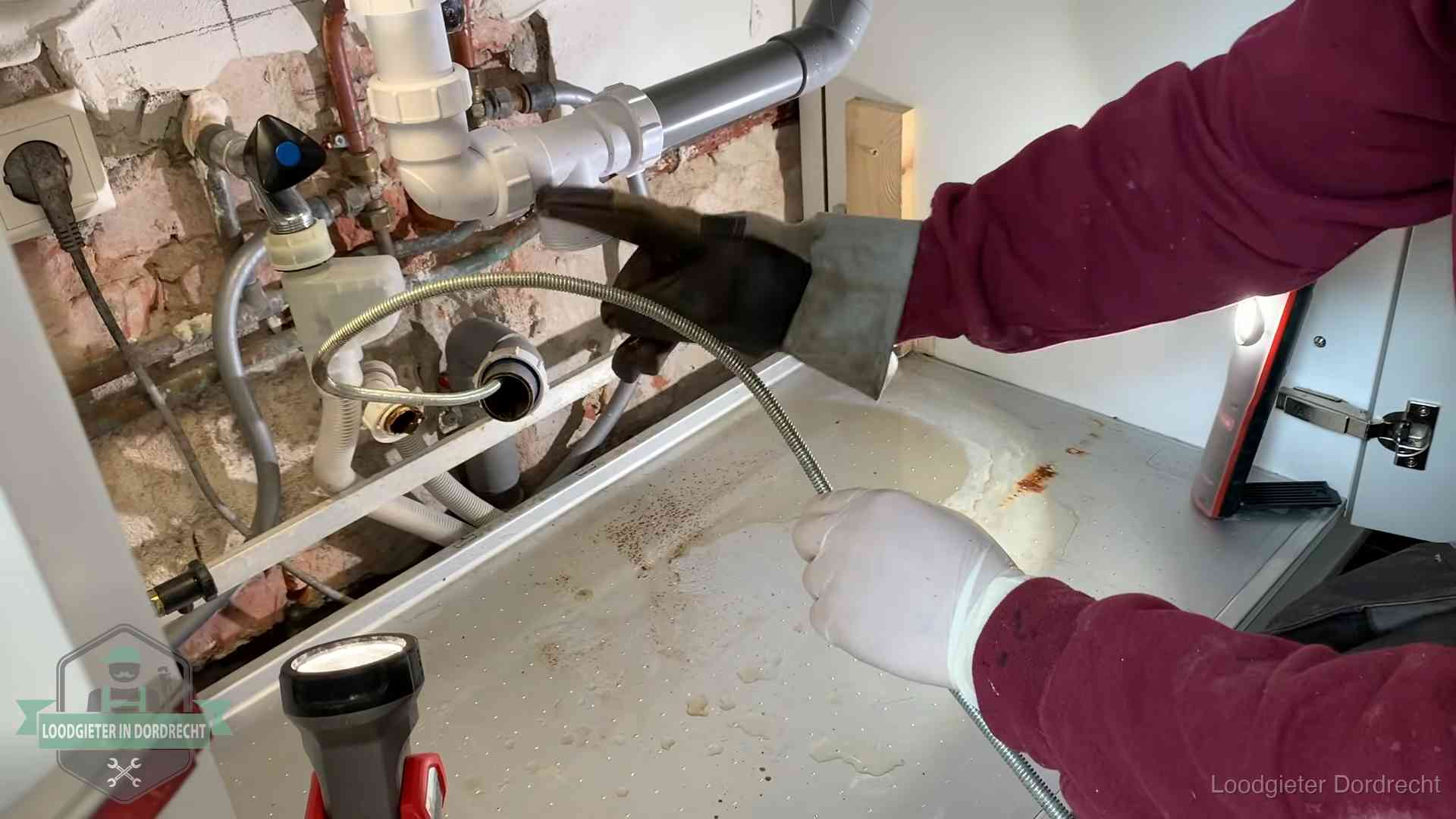 Ontstoppingsveer gaat in een geopende sifonaansluiting onder het aanrecht in Dordrecht