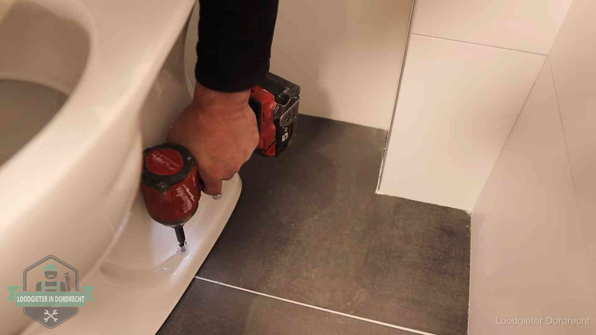 Kosten wc ontstoppen in Dordrecht Loodgieter zet de voet van een wc-pot vast op de tegelvloer in Dordrecht